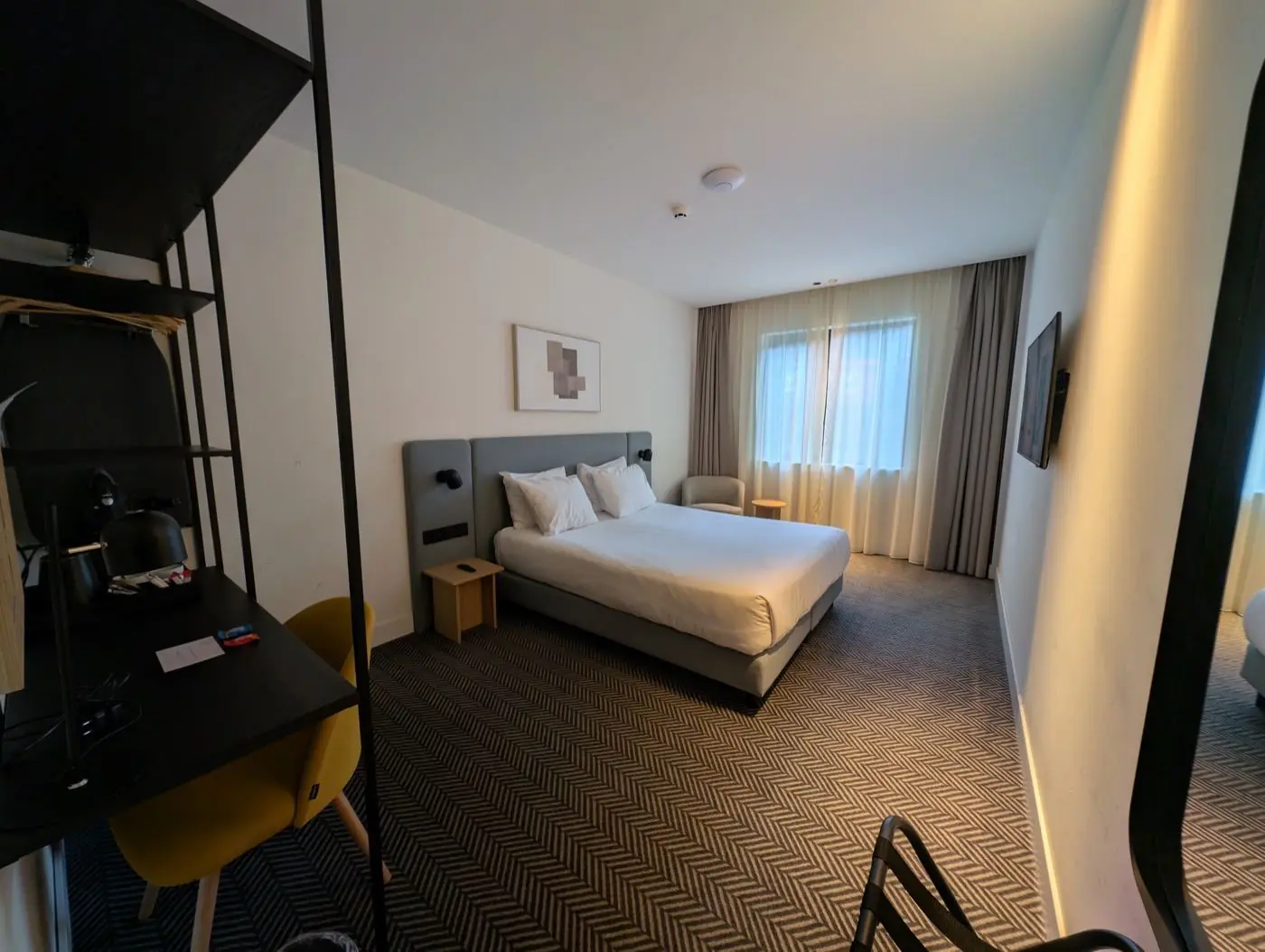 A modern hotel bedroom with a queen bed, white bedding and bedside lamps